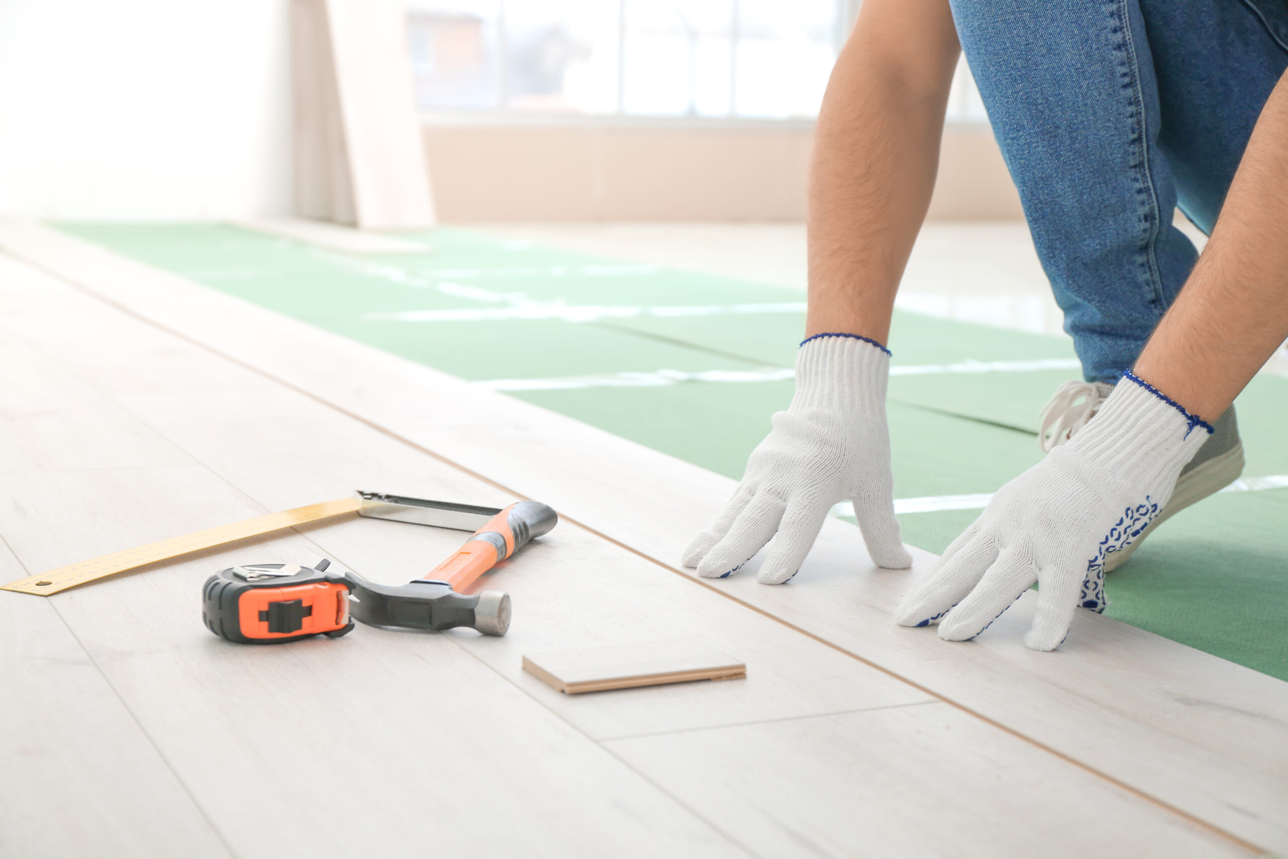 Carpenter installing laminate flooring in room